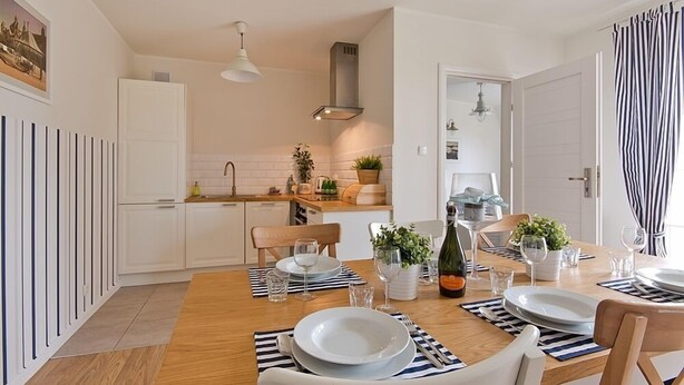 A modern kitchen with white cabinets, a wooden dining table set for four, and a hanging light fixture. - Imperial Apartments - Valor (Sopot)
