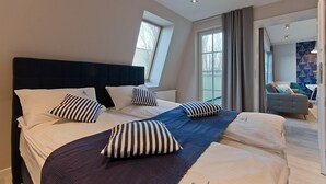 A modern bedroom with a large bed, two windows, a view of the outdoors, and a separate seating area with a sofa and table. - Imperial Apartments - Valor (Sopot)
