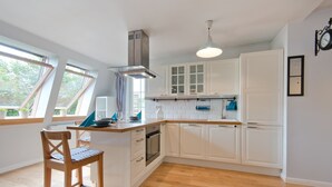 A modern kitchen with white cabinets, a wooden dining table, and a built-in oven. - Imperial Apartments - Valor (Sopot)