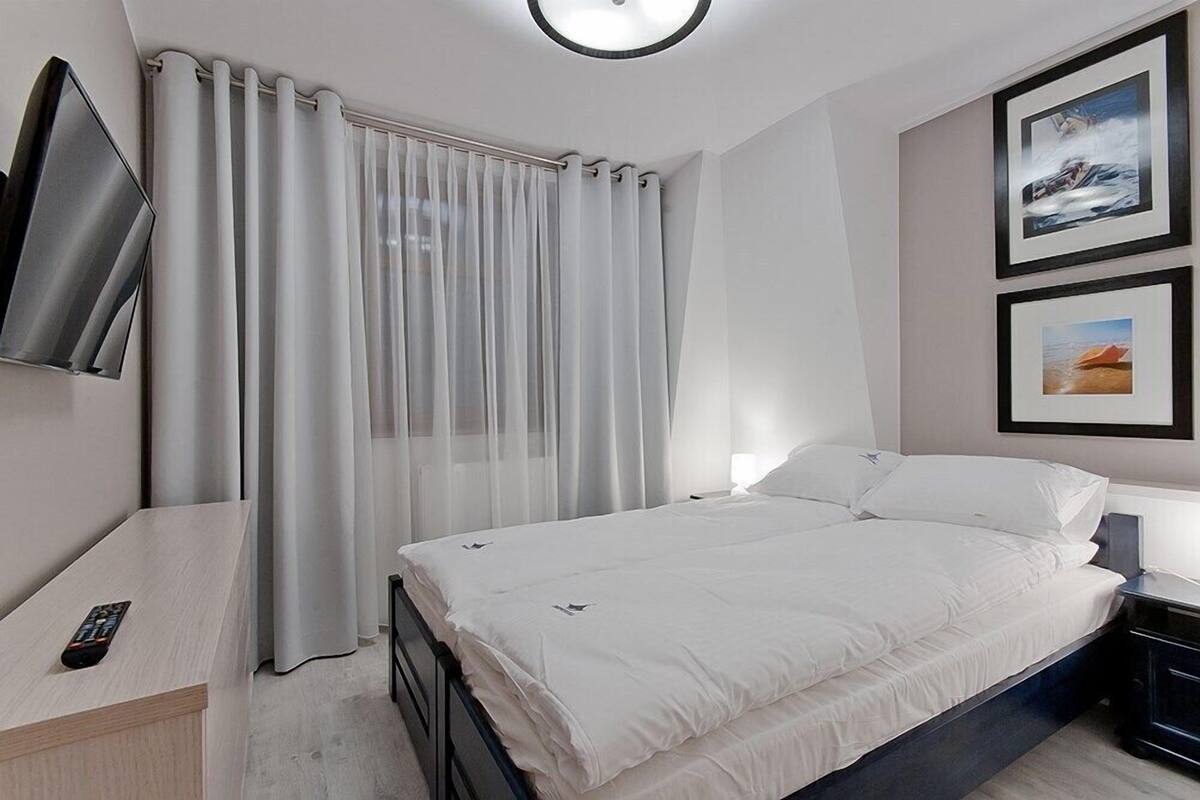 Une chambre d’hôtel moderne, équipée d’un lit, d’un téléviseur fixé au mur et de deux tableaux encadrés.