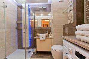 A modern bathroom with a glass-enclosed shower, a sink with a towel, and a washing machine.