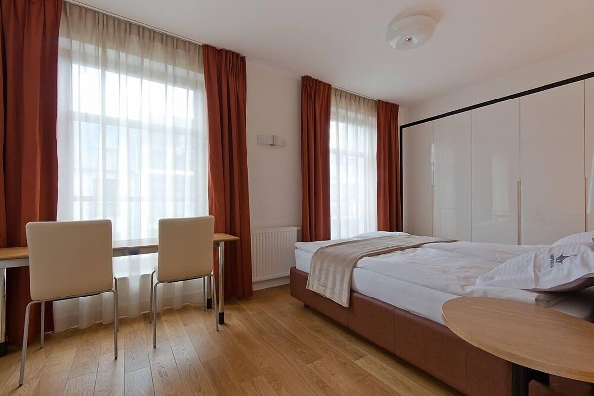 Une chambre d’hôtel avec un lit, deux chaises, une petite table et un radiateur.