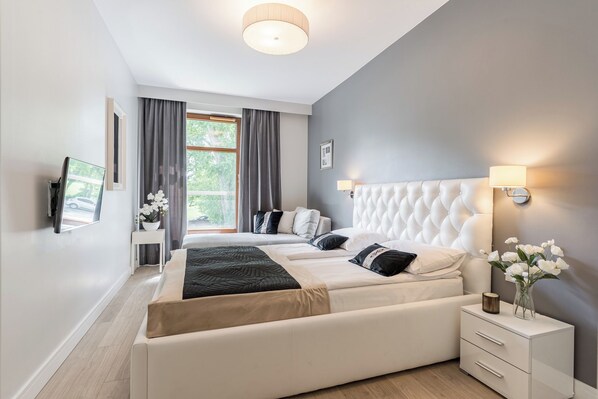 A modern bedroom with a large bed, bedside tables, a wall-mounted TV, and a window with curtains.
