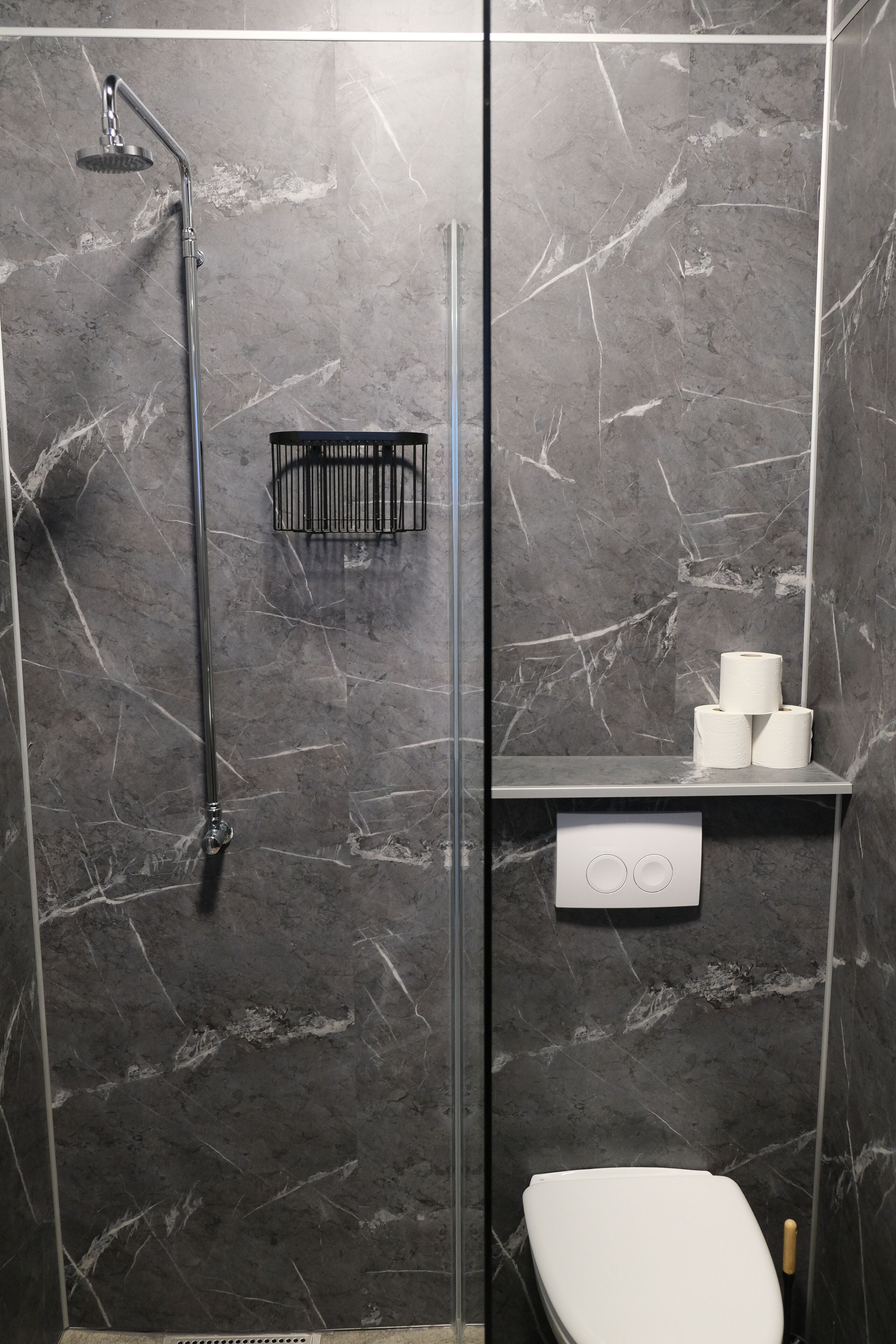 Un baño moderno con ducha de vidrio, inodoro y repisa con artículos de aseo.