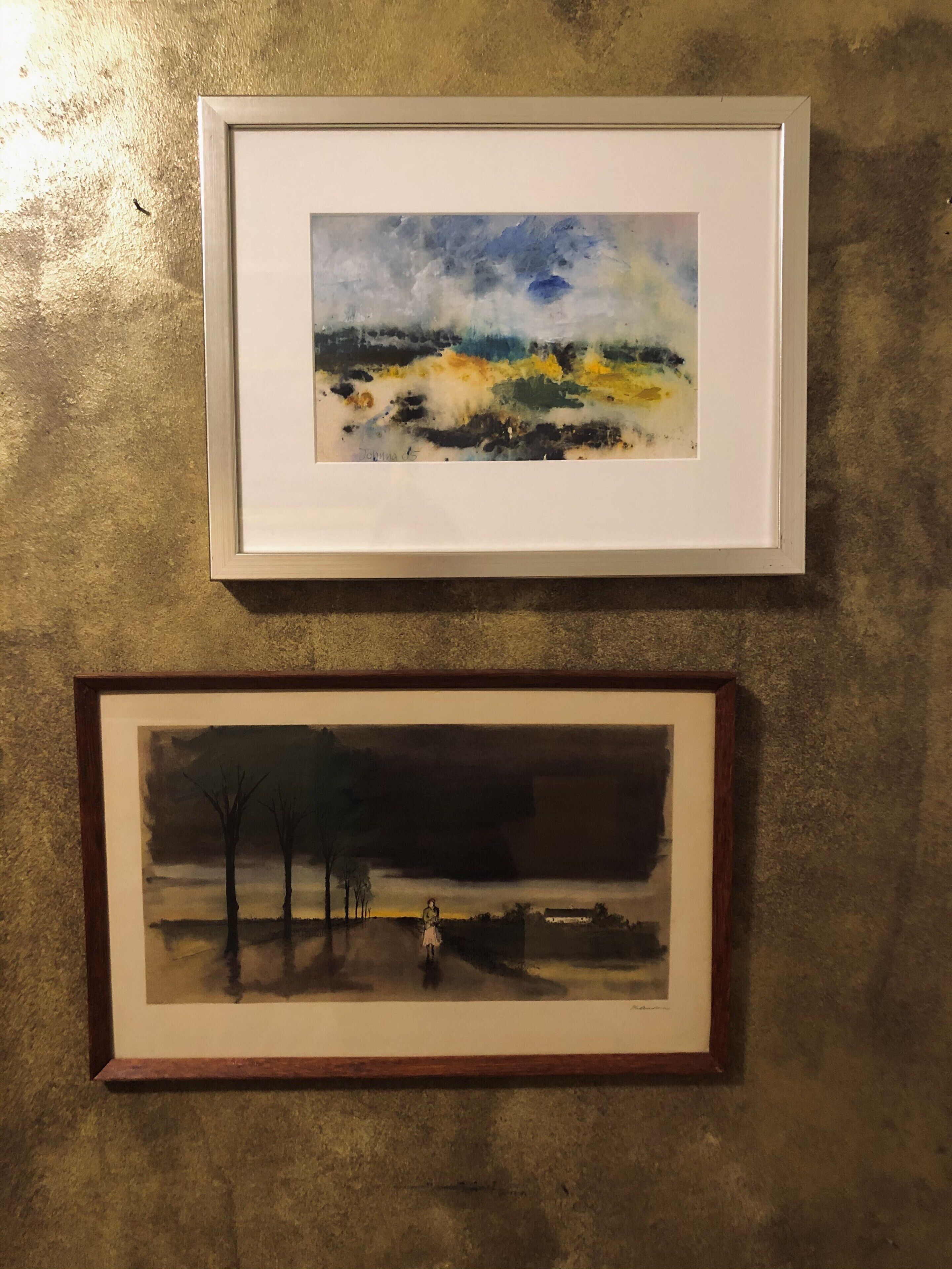 Two framed paintings on a textured wall.