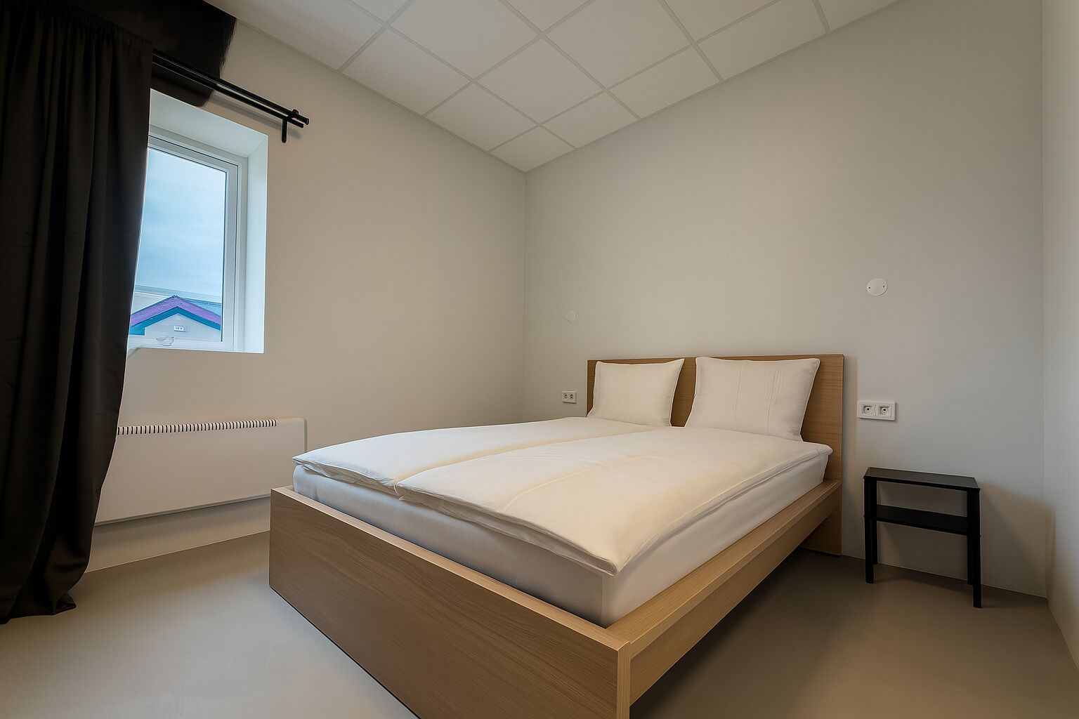 Un dormitorio con cama, ventana, radiador y una mesita.