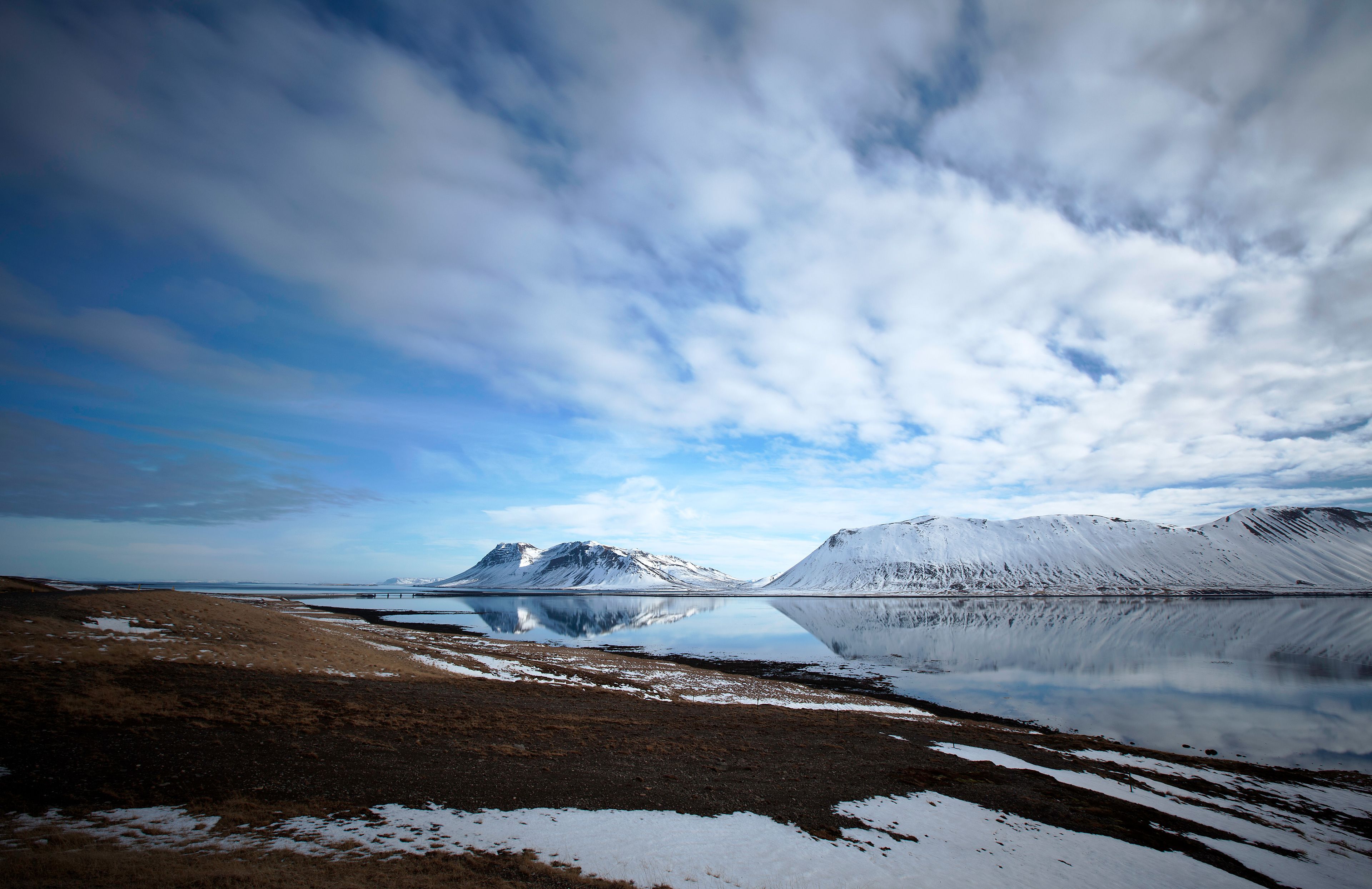 A tranquil landscape with a clear sky, snow-covered mountains, and a calm body of water reflecting the scenery.