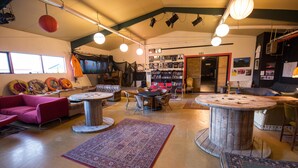 A cozy interior with round tables, a sofa, and a bookshelf filled with books. - The Freezer Hostel & Culture Center (Rif)