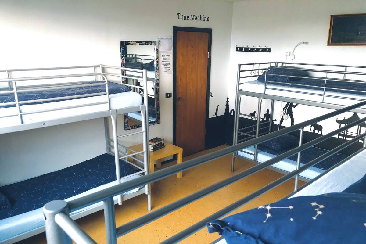 A dormitory room with bunk beds, a small table, a door, and a wall with a poster.