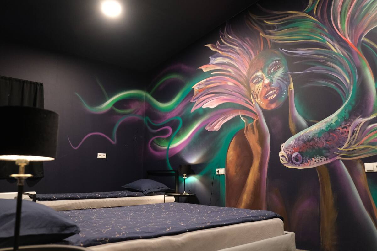 A bedroom with a bed, a nightstand, a lamp, and a mural on the wall.