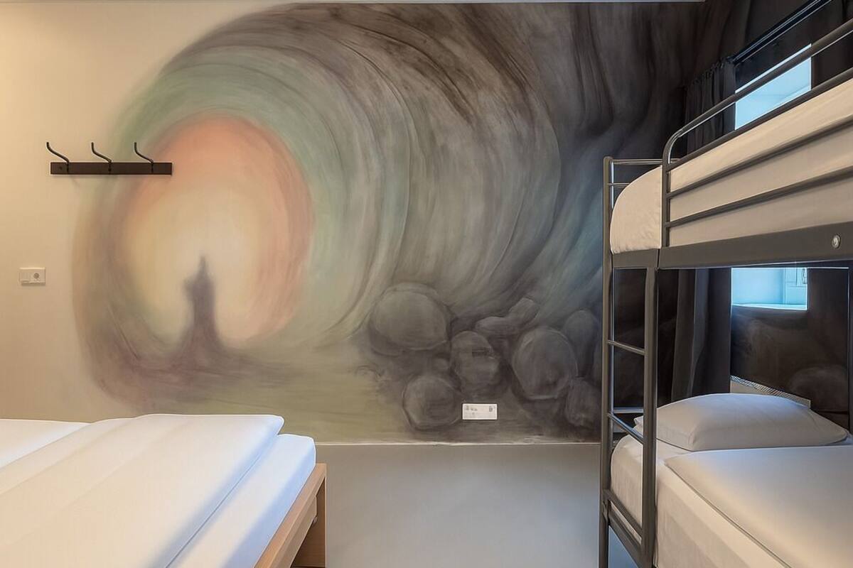 A room with bunk beds, a mural on the wall, and a small window.