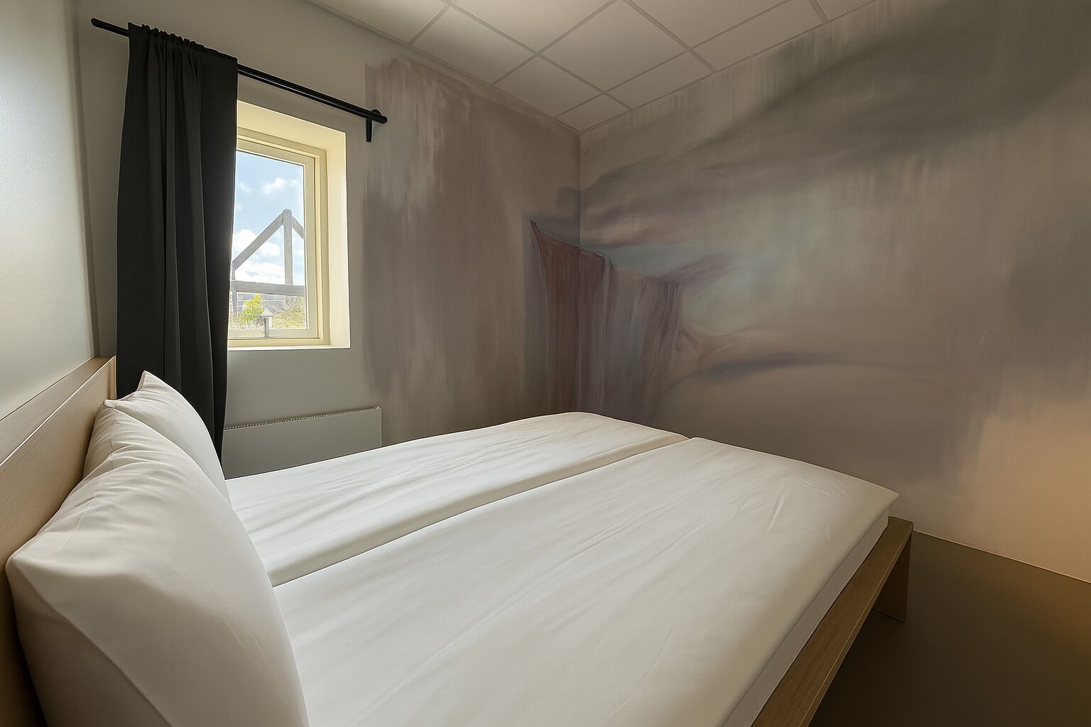 Een slaapkamer met een enkel bed, een raam met gordijnen en uitzicht op buiten.