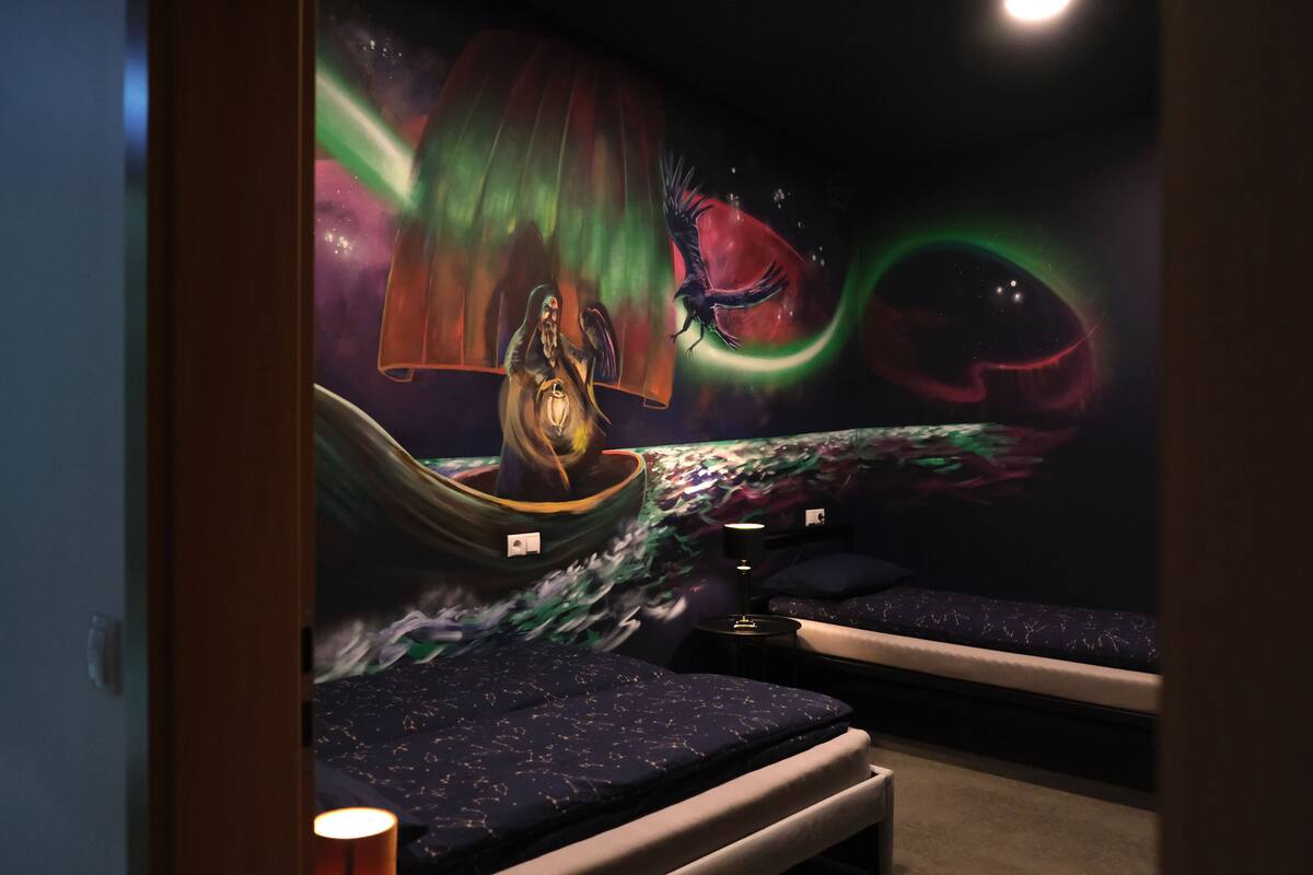 A room with a mural of a figure in a boat, a bed, and a nightstand with a lamp.