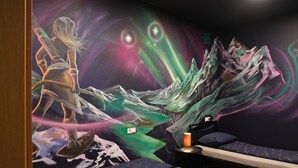 A room with a mural of a cosmic scene, a bed, a nightstand, and a lamp. - The Freezer Hostel & Culture Center (Rif)