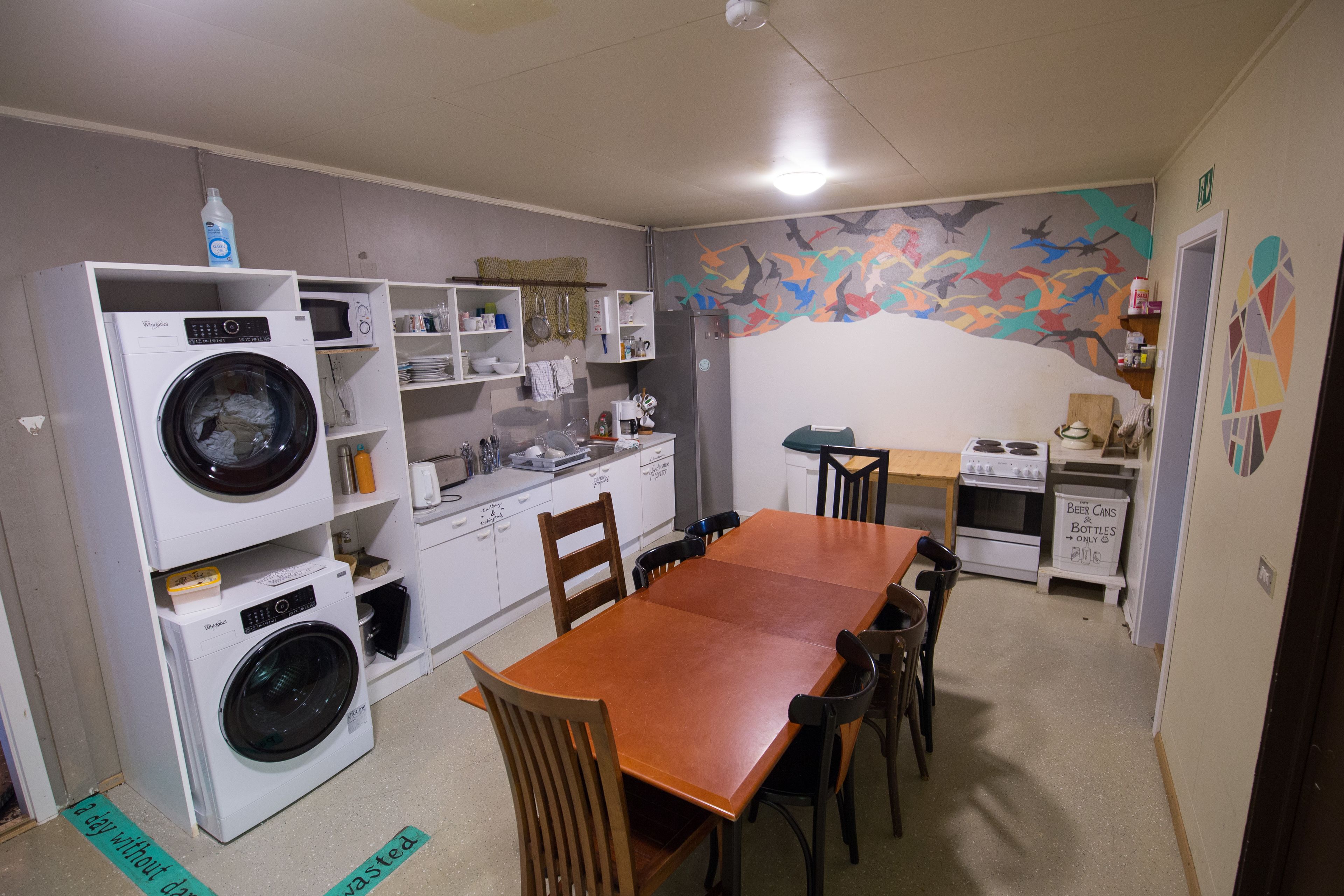 A compact kitchen with a dining table, chairs, a washing machine, and a microwave.