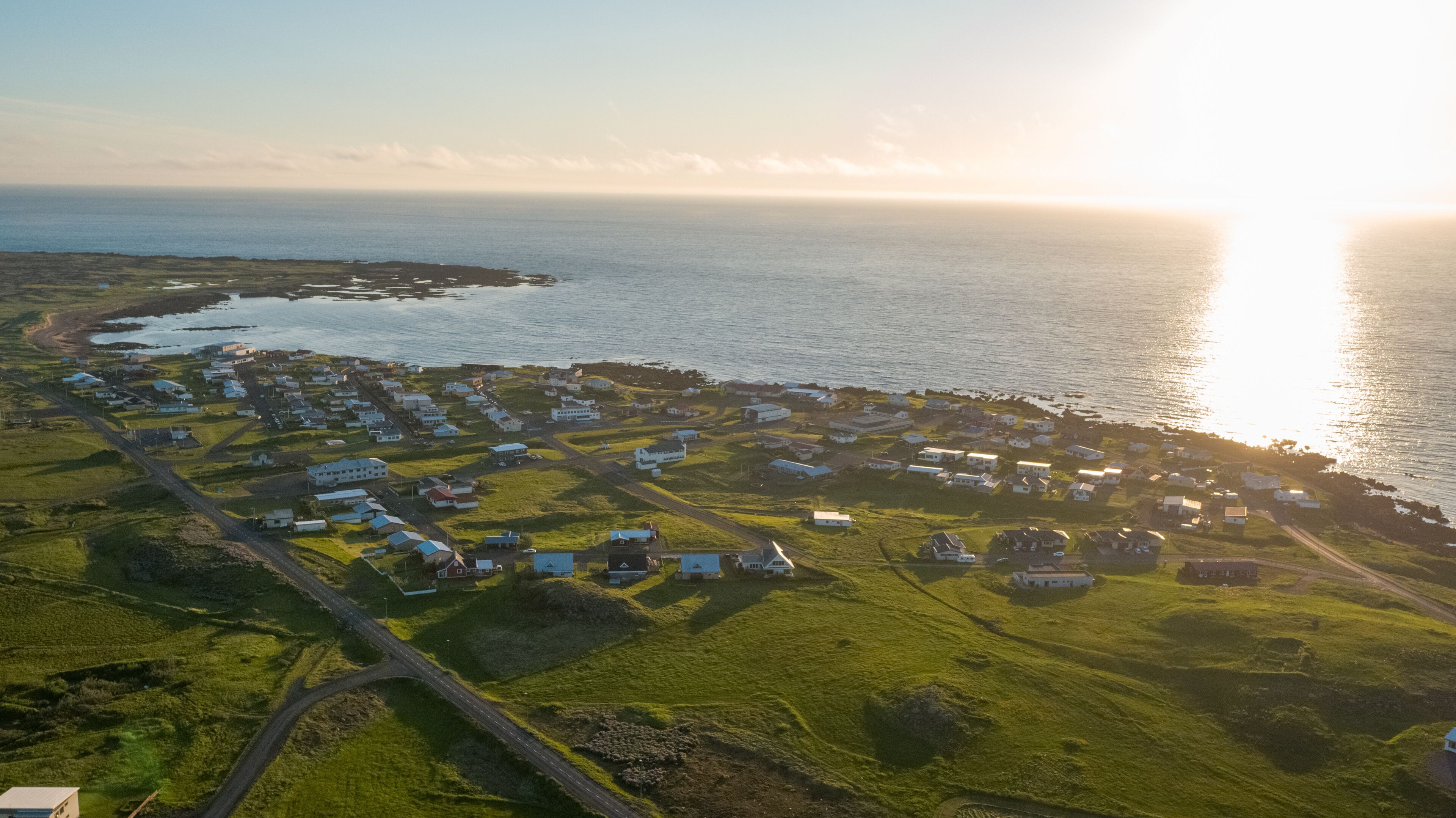 An aerial view of a coastal village with houses and a road leading to the sea.