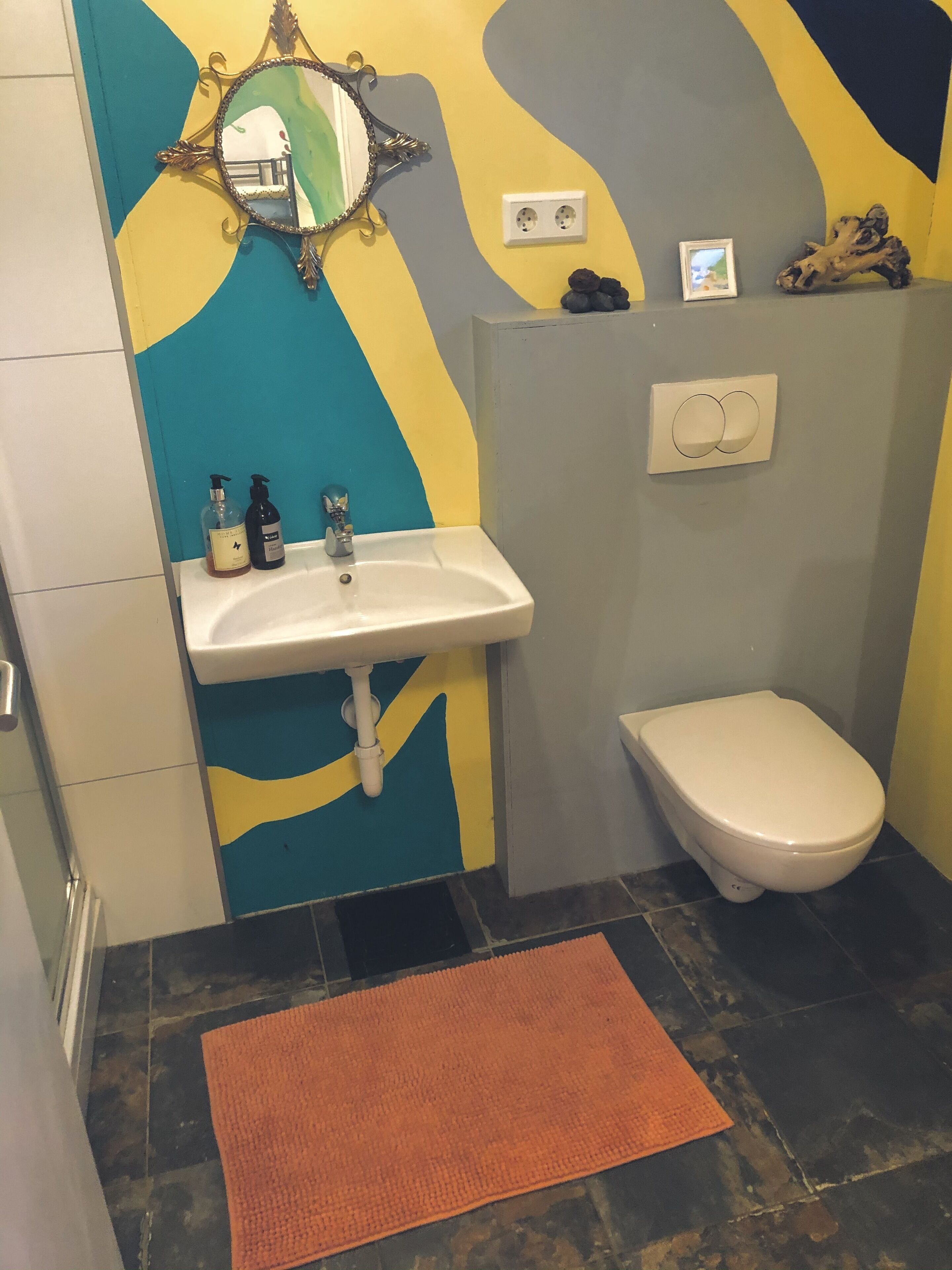 A bathroom with a sink, mirror, toilet, and a decorative wall.