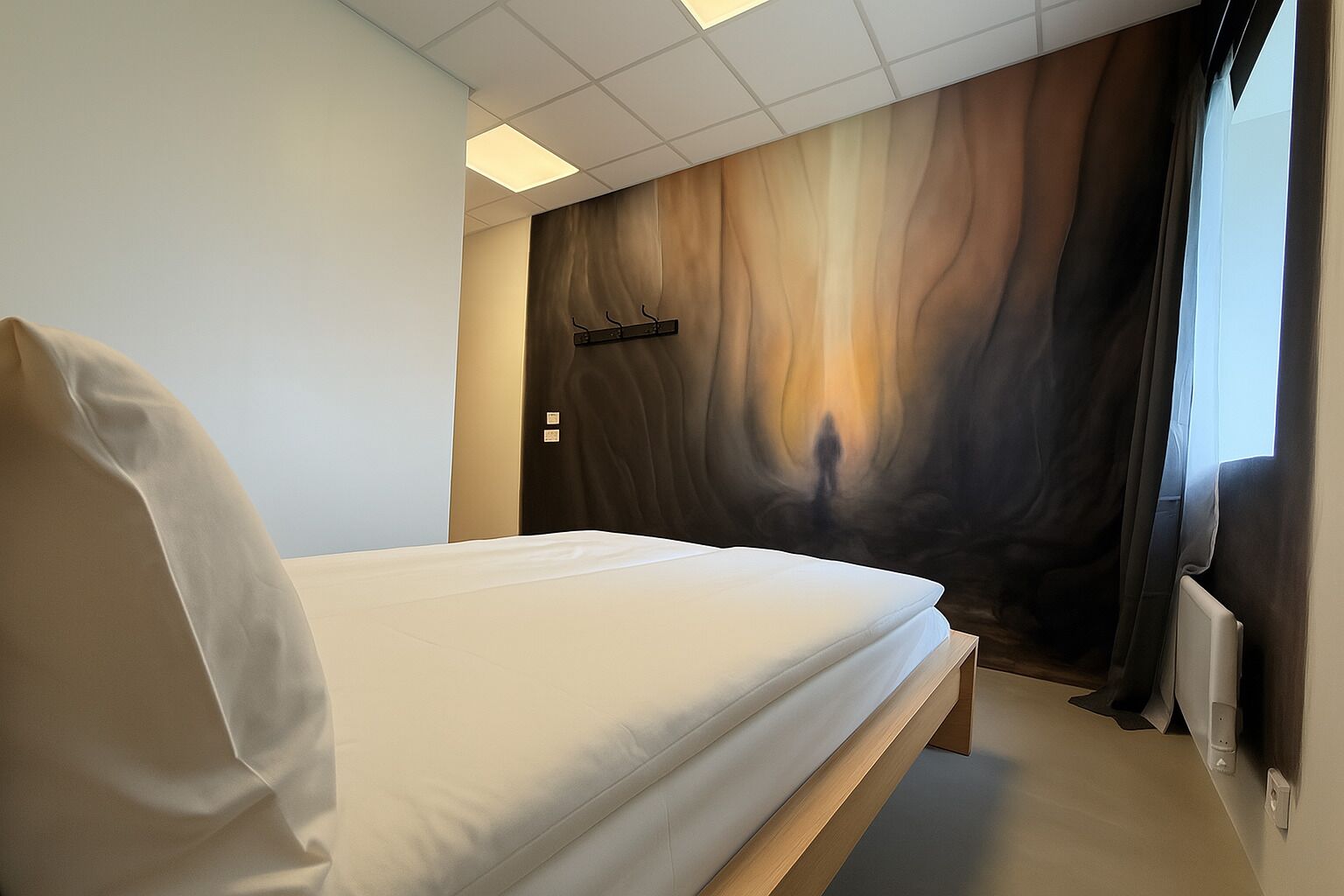 A modern hotel room with a bed, a wall-mounted coat rack, and a large window with curtains.