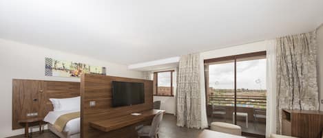 Una habitación de hotel moderna con cama, escritorio, televisor, balcón con vistas y zona de comedor.