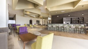 A spacious lobby with a modern bar area, comfortable seating, and a high ceiling with geometric patterns.