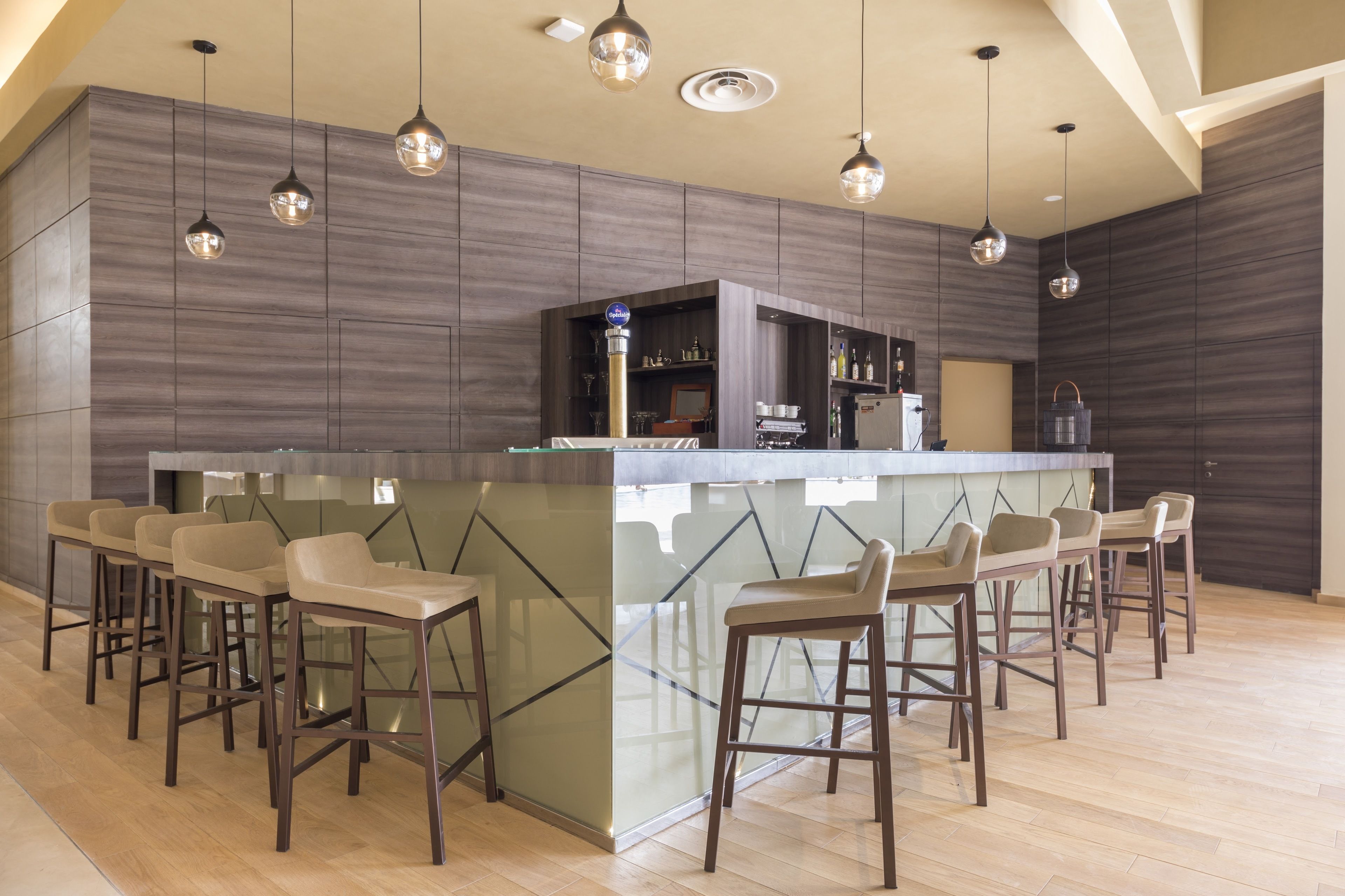 Un espace bar moderne doté d’un comptoir avec un plateau en verre et de plusieurs tabourets.