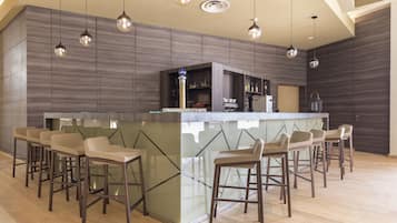 Un espace bar moderne doté d’un comptoir avec un plateau en verre et de plusieurs tabourets.