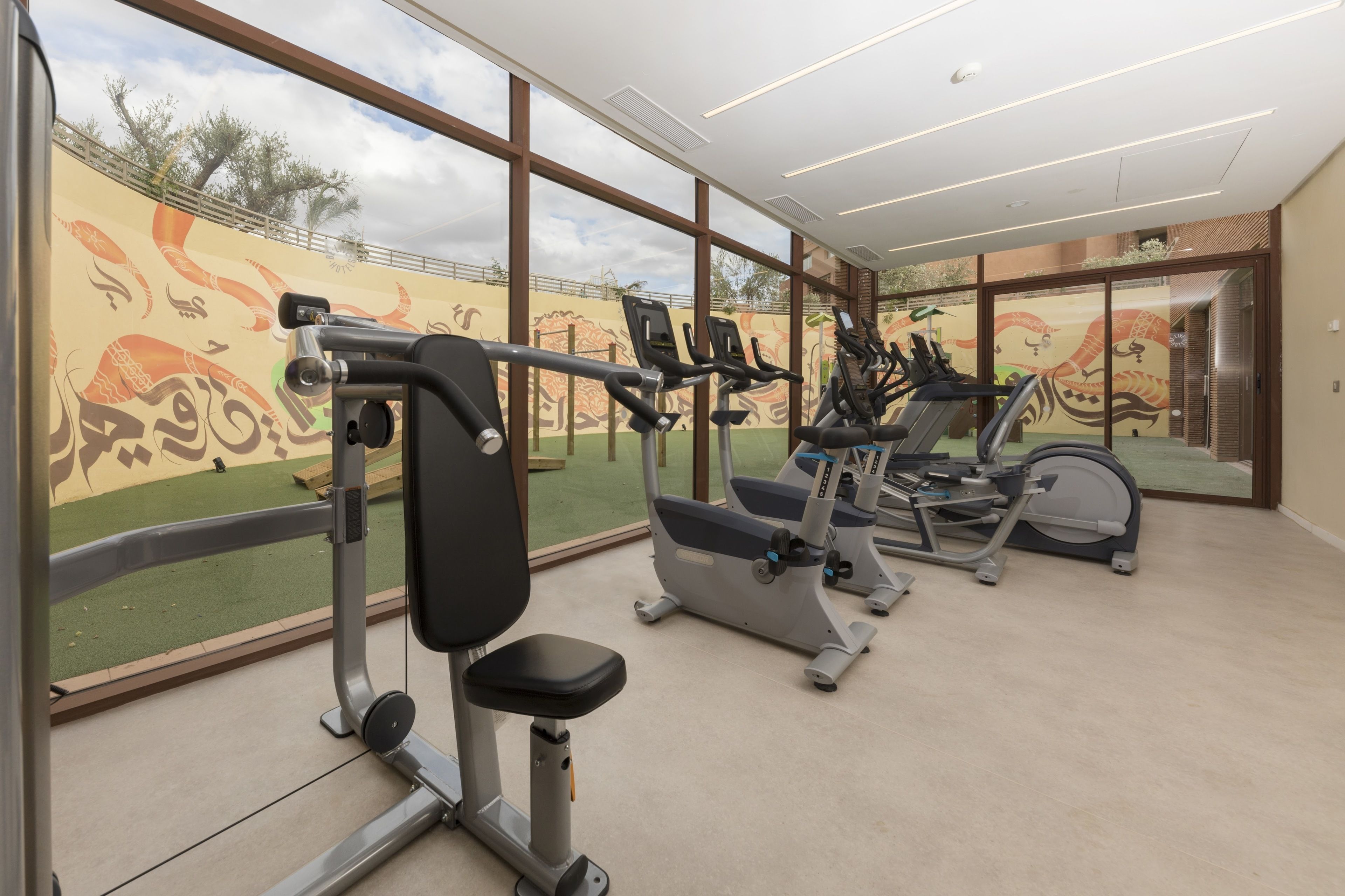 Une salle de sport équipée de matériel d’exercice, dotée de grandes fenêtres et ornée d’une fresque murale.
