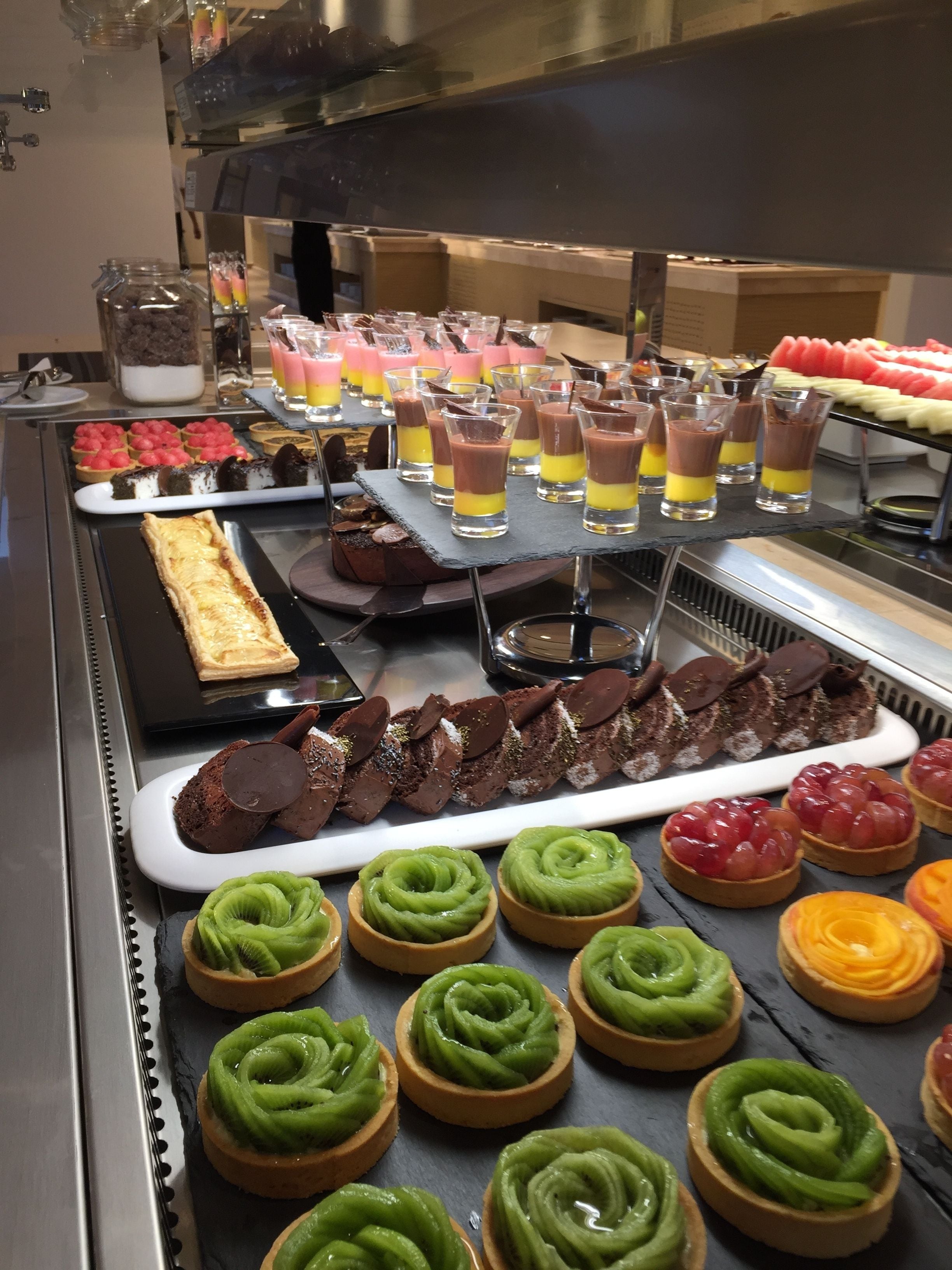 A buffet with various desserts including chocolate tarts, fruit tarts, and layered drinks.