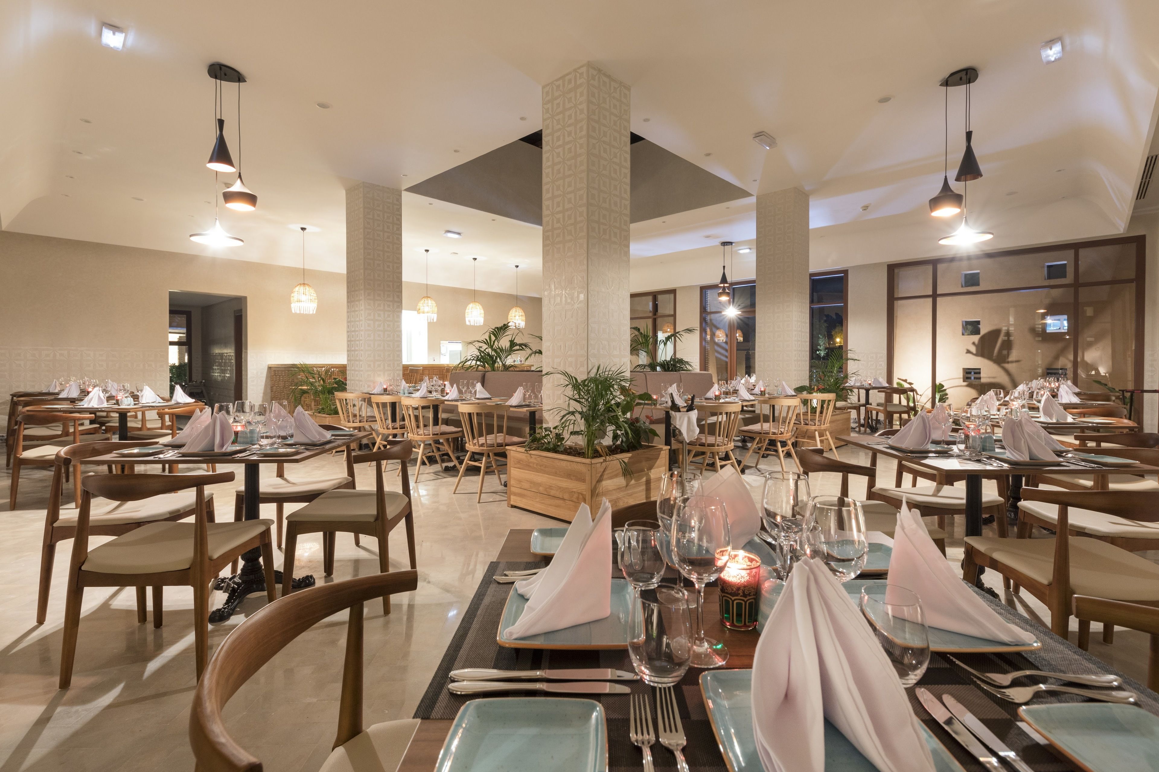 A spacious dining area with multiple tables set for dining, featuring wooden chairs and a central plant display.