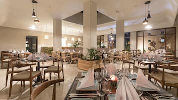 A spacious dining area with multiple tables set for dining, featuring wooden chairs and a central plant display.