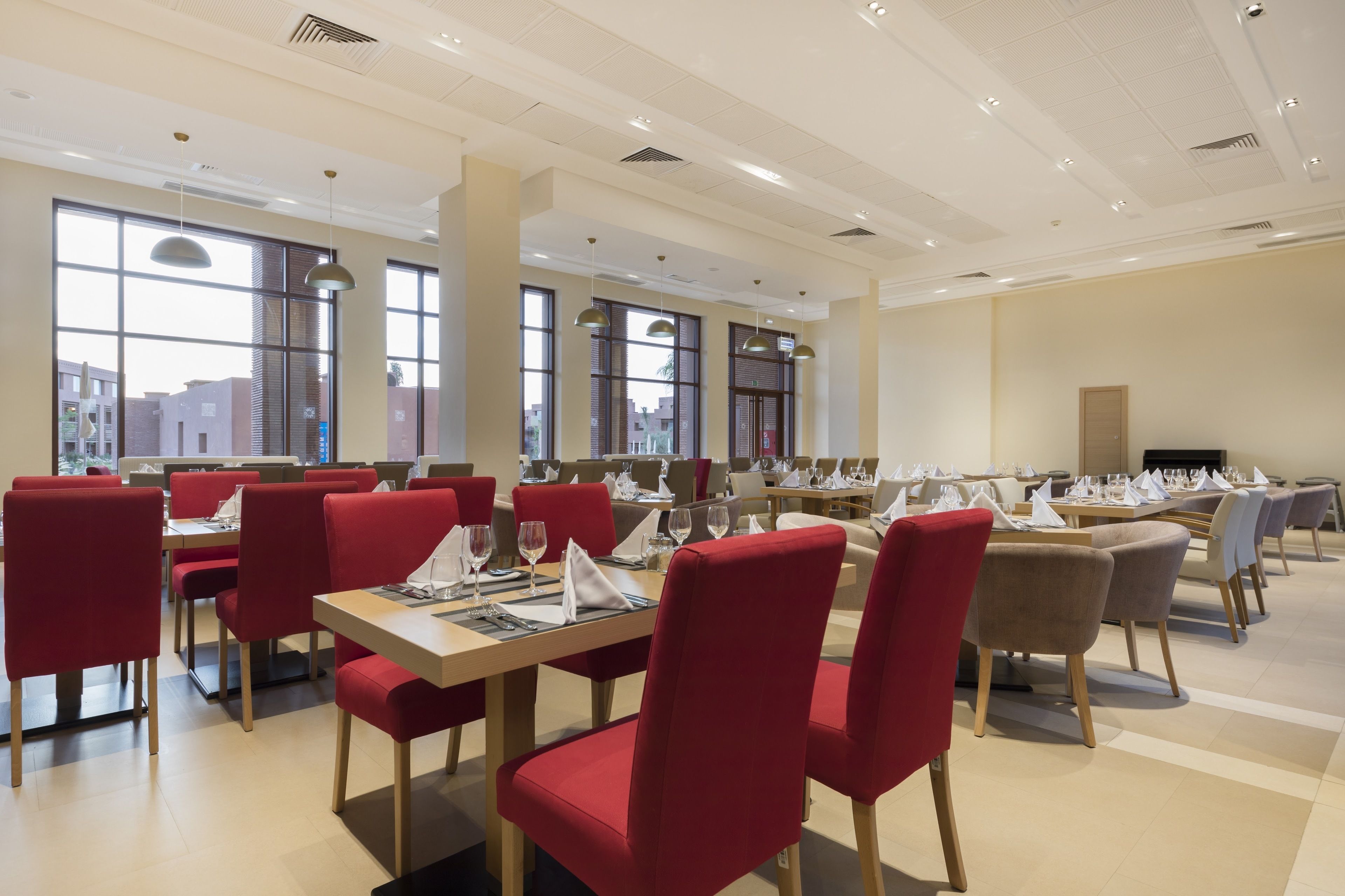 Un comedor amplio con varias mesas y sillas, ventanas grandes y un diseño moderno de techo.