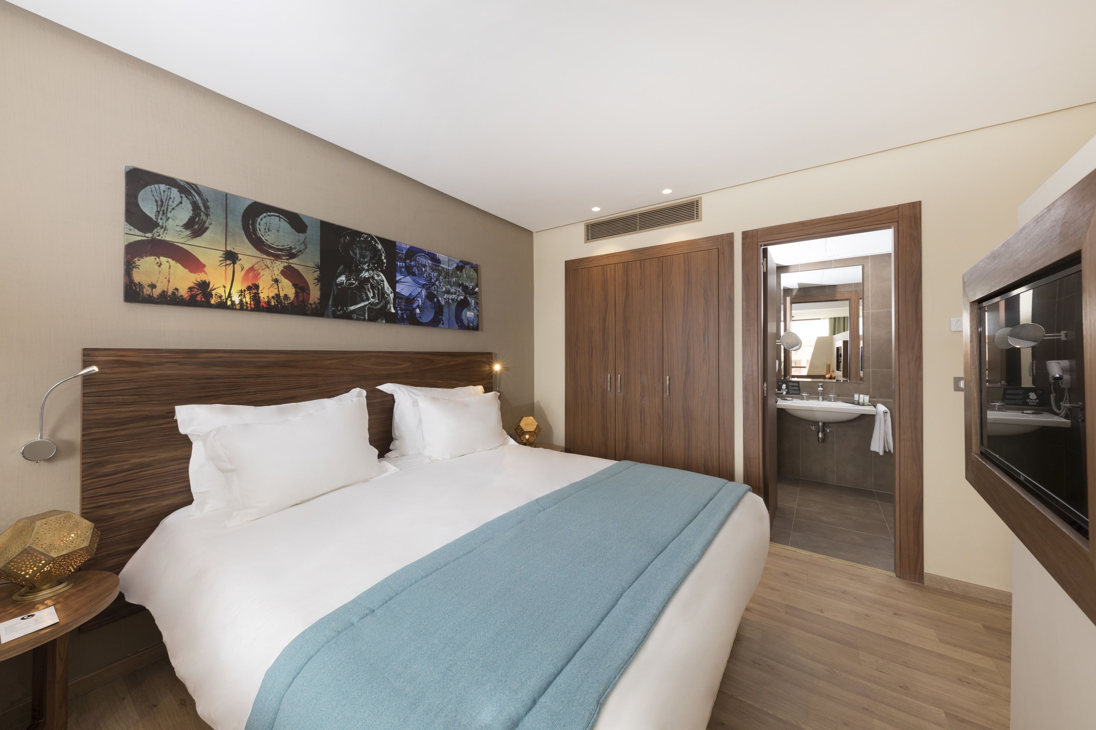 A hotel room with a large bed, a nightstand, a wall-mounted TV, and a bathroom visible through an open door.