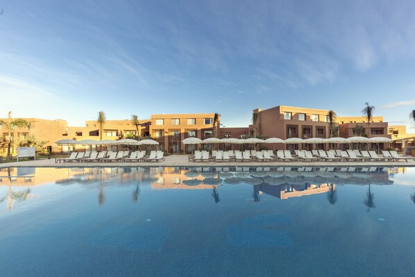 Una piscina con sillas de descanso y sombrillas, que refleja edificios cercanos.