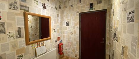 A bathroom with a mirror, a radiator, a fire extinguisher, and a door.