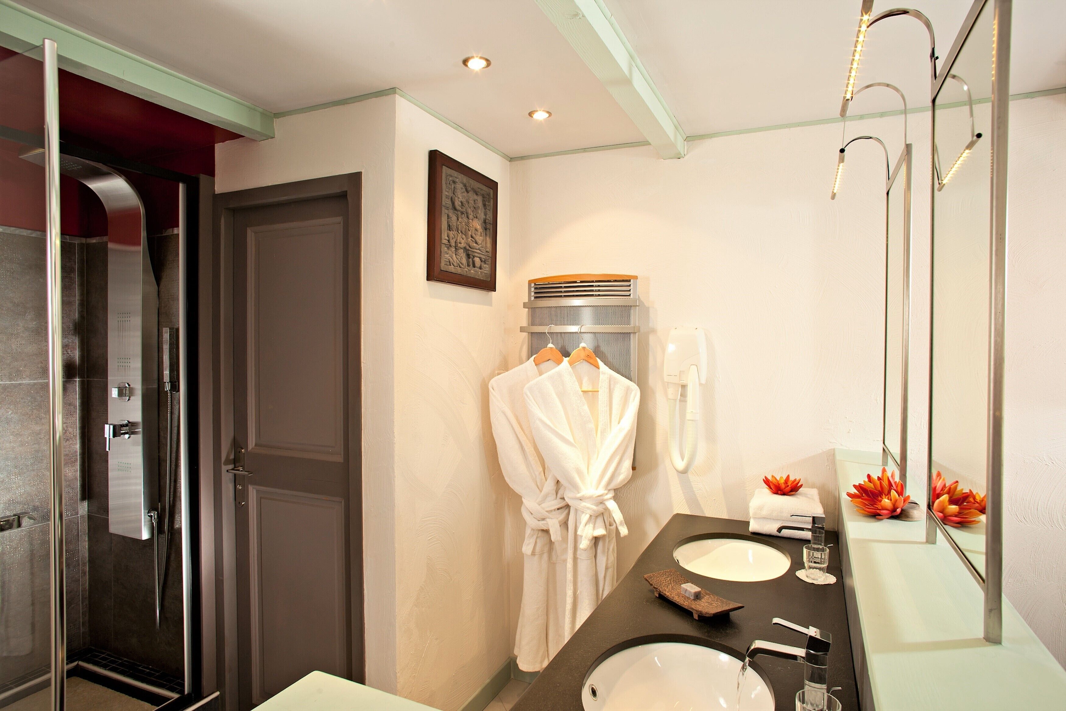 A modern bathroom with a glass shower enclosure, a vanity with a sink and mirror, and a robe hanging on the wall.