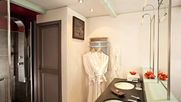 A modern bathroom with a glass shower enclosure, a vanity with a sink and mirror, and a robe hanging on the wall.