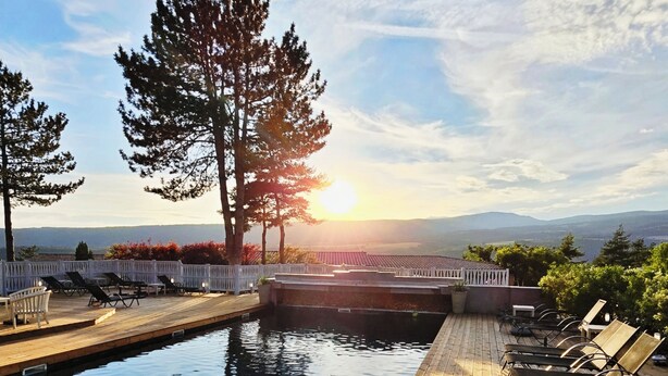 A wooden deck with a pool, lounge chairs, and a view of the sunset over mountains. - Domaine du Val de Sault (Sault)
