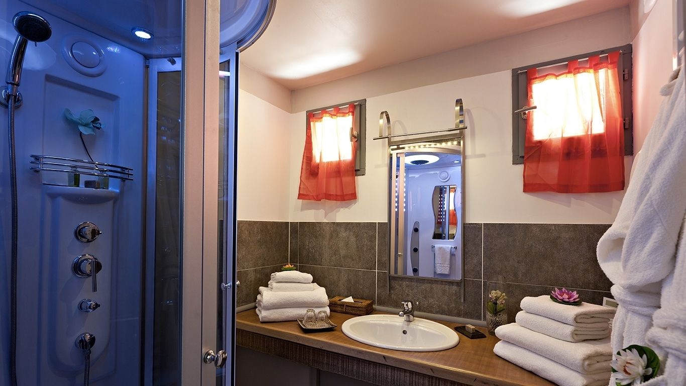 A bathroom with a shower, sink, and mirror. There are towels and toiletries visible.