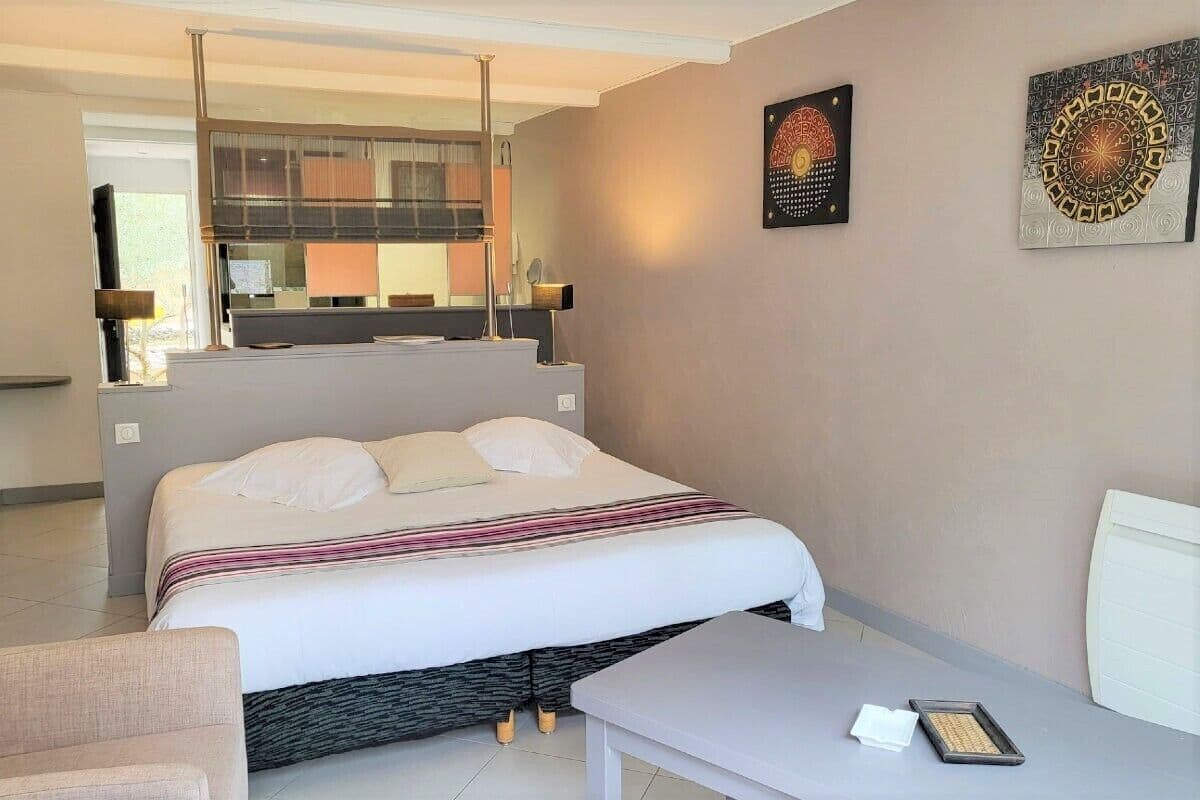 A hotel room with a bed, a chair, a table, and artwork on the walls.