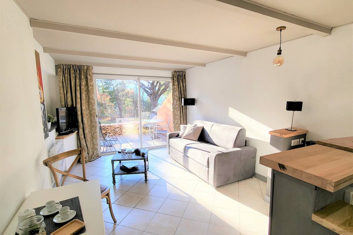 A modern living room with a sofa, coffee table, and a TV on a stand. There is a sliding glass door leading to an outdoor patio area.