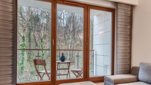 A room with a large sliding glass door leading to a balcony with a wooden chair and a small table. There is a cushioned bench in the room. - Imperial Apartments - Aquarius (Sopot)