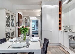 Une cuisine moderne avec des meubles blancs, un coin repas avec une table dressée pour deux personnes, et une vue sur la chambre.