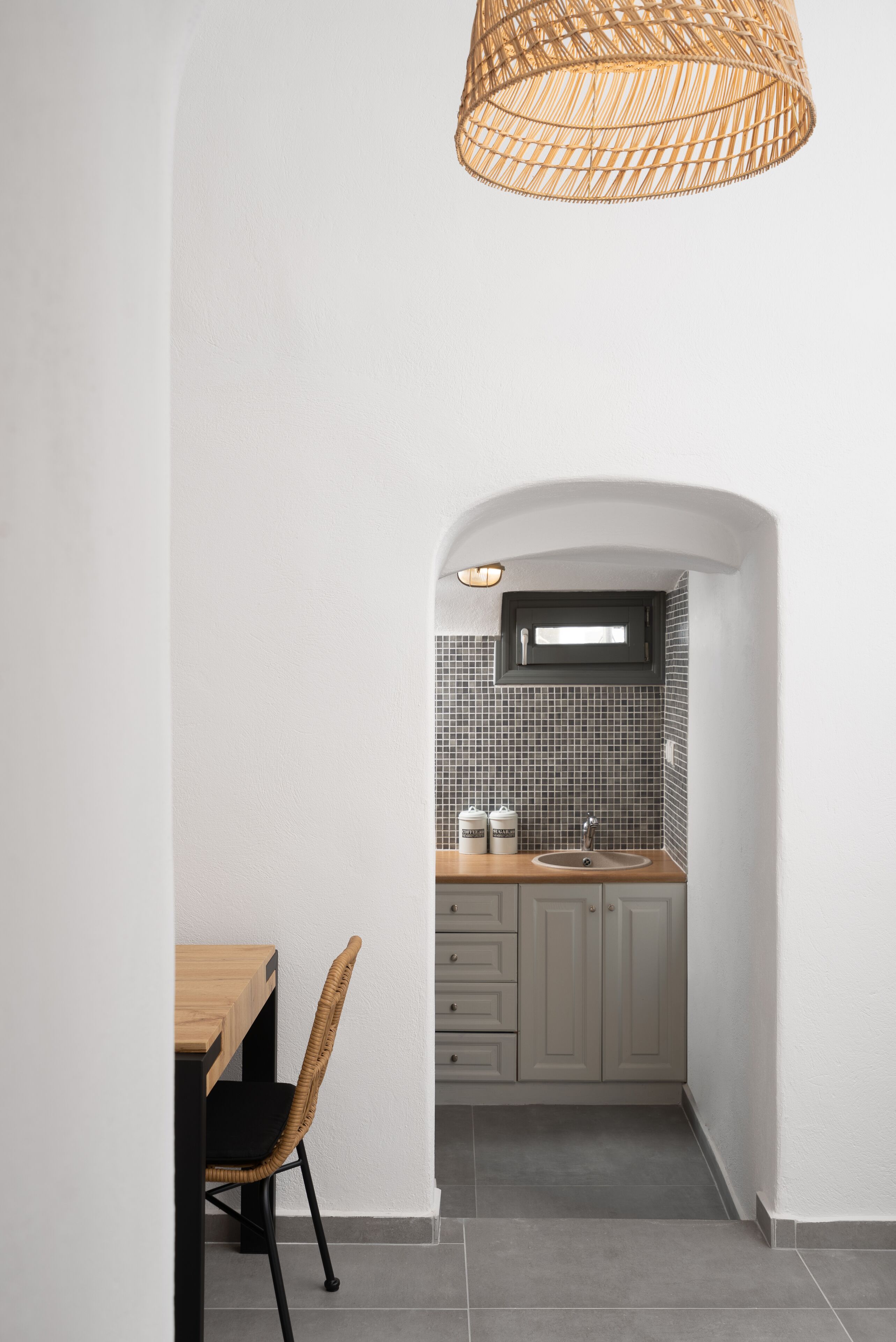 Une cuisine avec un mur recouvert de carreaux, une table en bois et une chaise en osier.