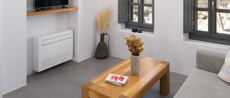 Un salon moderne avec un téléviseur posé sur une étagère, une table basse en bois, un canapé et deux fenêtres équipées de volets.