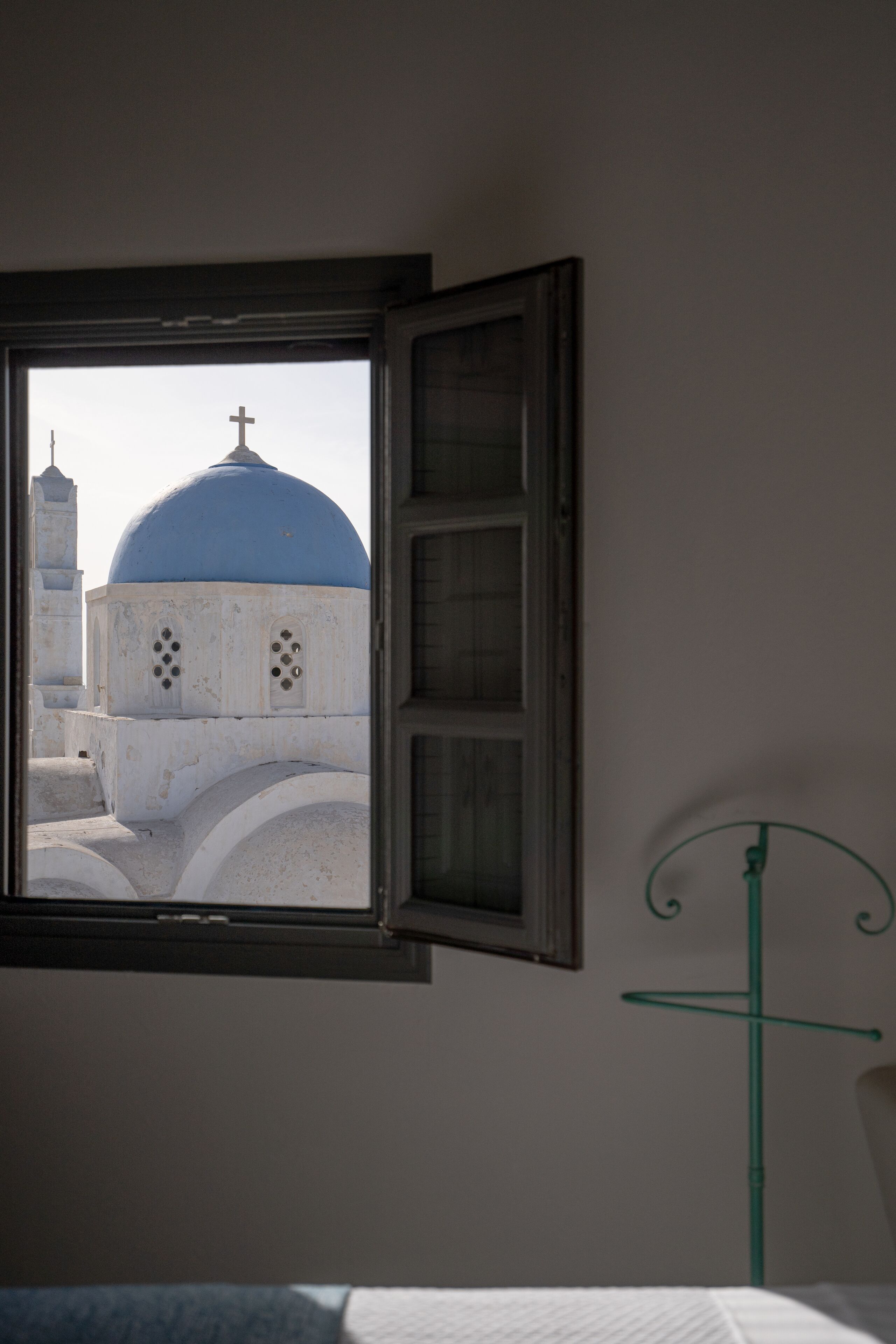 A window with a view of a building with a blue dome and a cross, a metal stand, and a white wall.