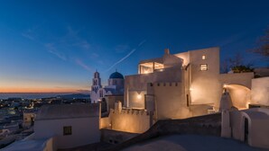 A coastal building with a prominent dome and a cross on top, surrounded by a fortified wall. - Kastro Mansion (Santorini)