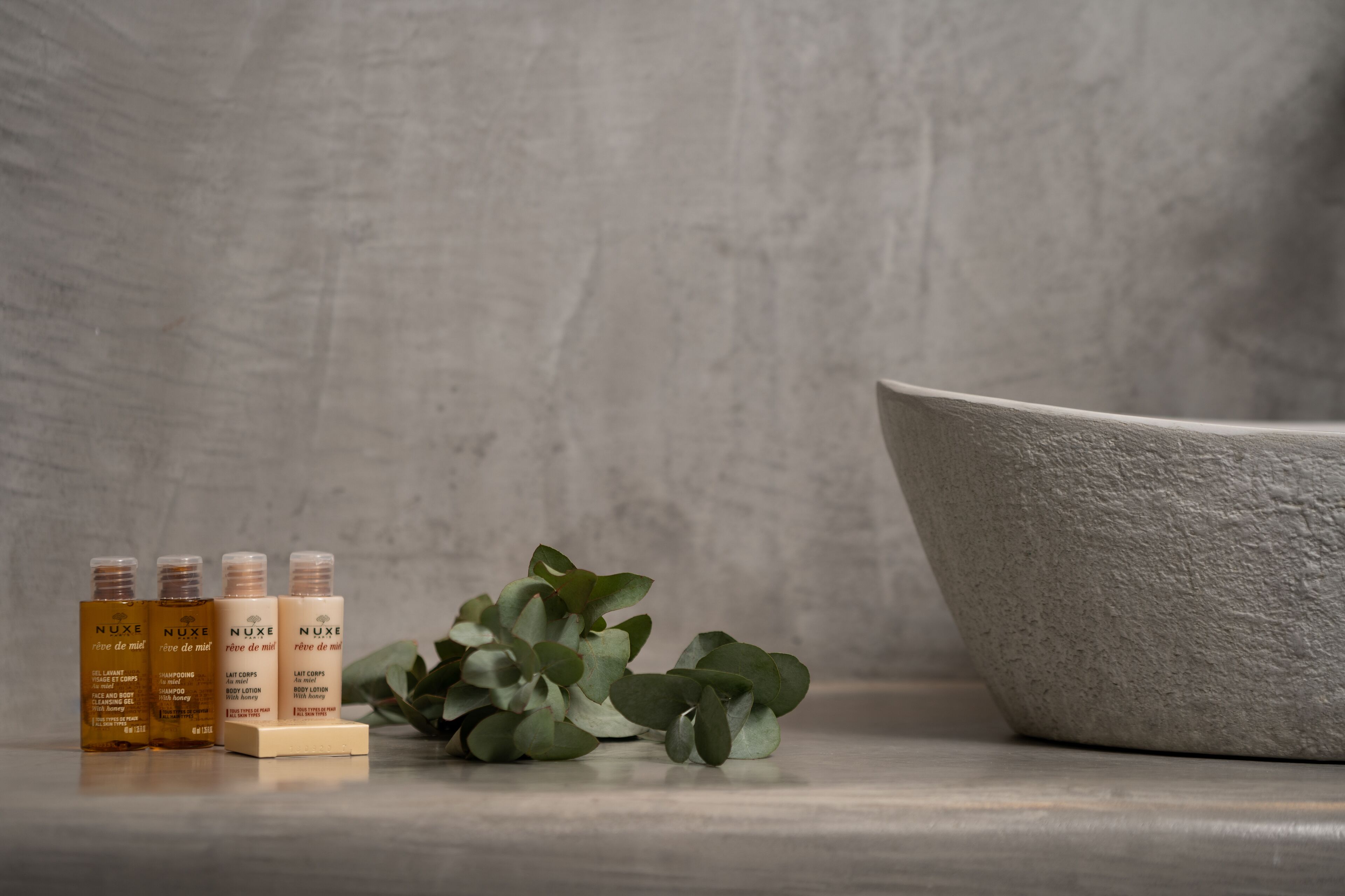 Four Nuxe skincare bottles and a bowl on a marble surface.