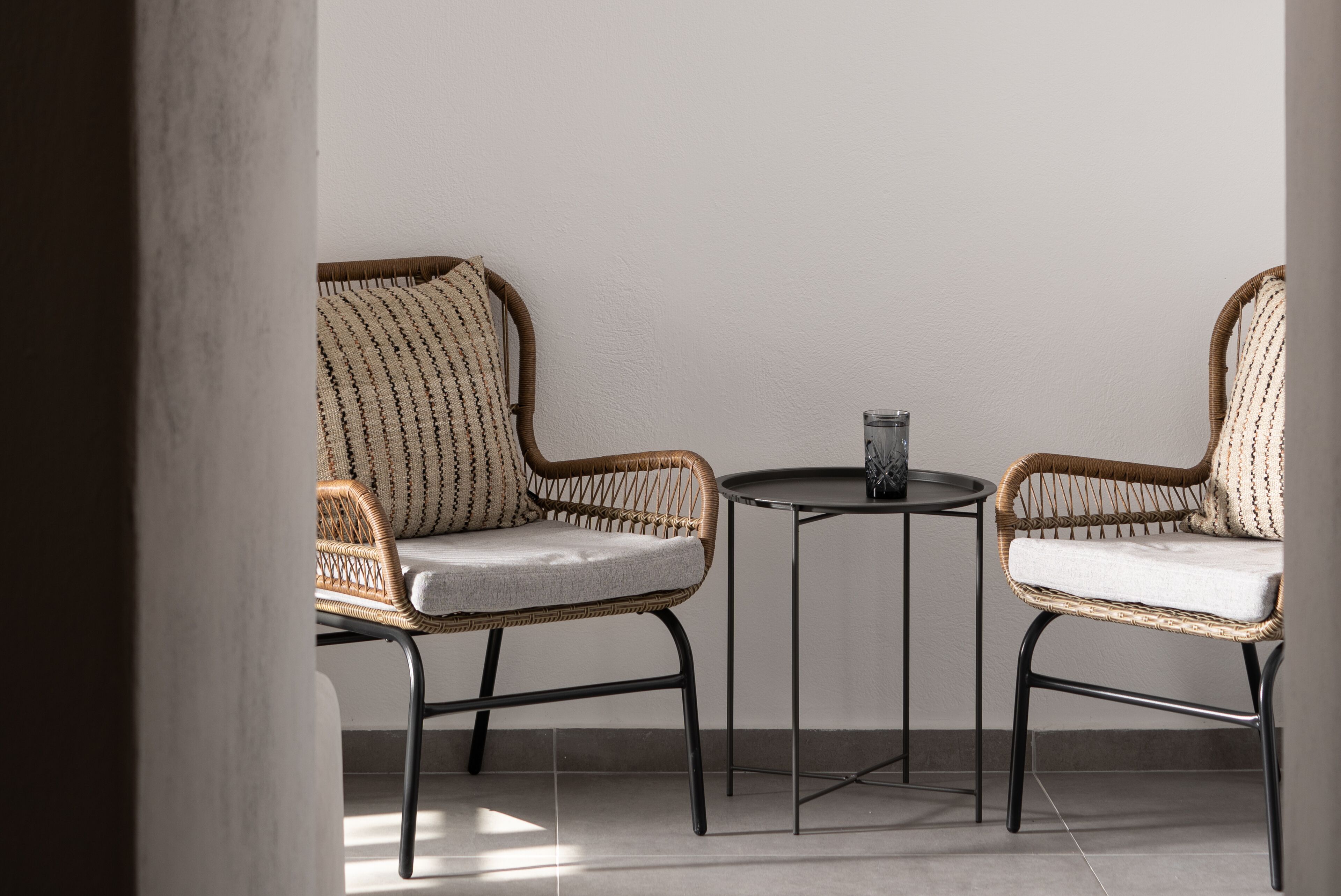 Two wicker chairs with cushions, a small round table, and a glass of water.