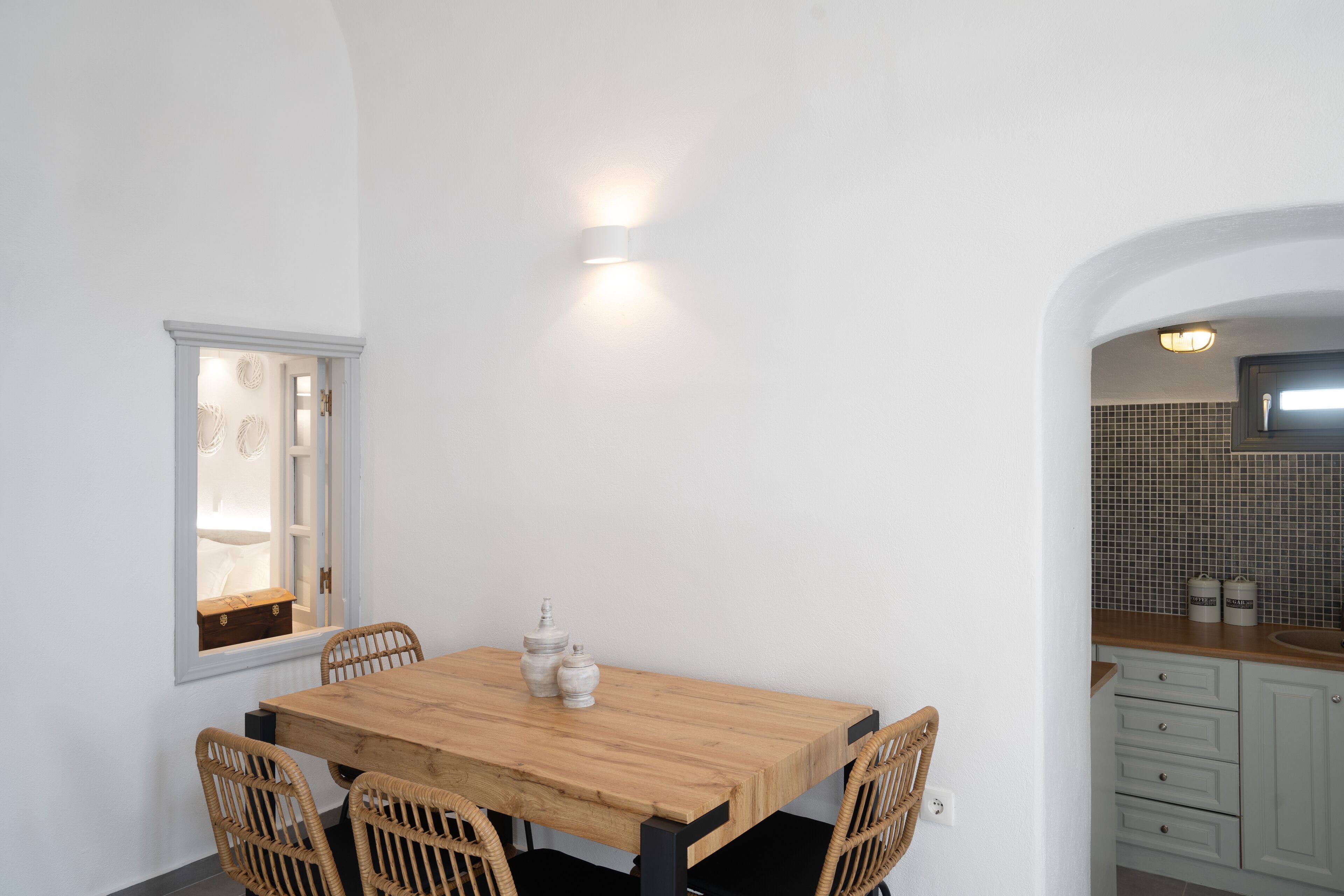 Un comedor con mesa de madera y sillas de mimbre, pared blanca y ventana con vistas.