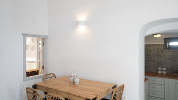 Un comedor con mesa de madera y sillas de mimbre, pared blanca y ventana con vistas.
